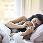 Woman Lying on Bed While Blowing Her Nose